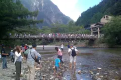 Summer visitors beside the Azusa River and Kappa Bridge with green mountain slopes behind