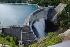 Curving Kurobe Dam wall releasing water beside the reservoir